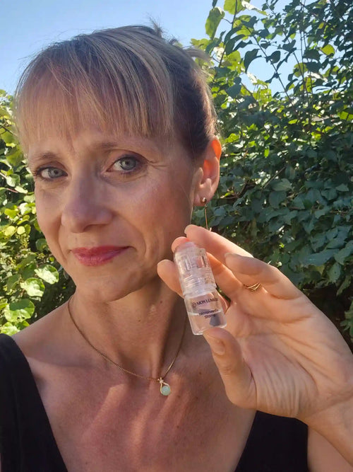 Woman holding a small bottle outdoors with greenery in the background