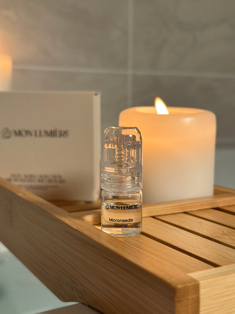 Small bottle of Mon Lumiere product on a wooden tray with a lit candle in the background.