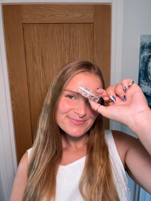 Woman holding a small bottle of perfume up to her eye in a room with a wooden door.